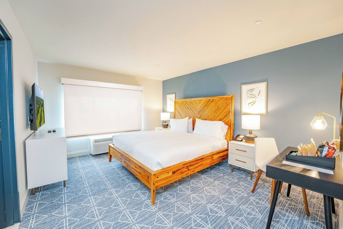 A modern hotel room with a large bed, bedside tables, a desk, and a TV.