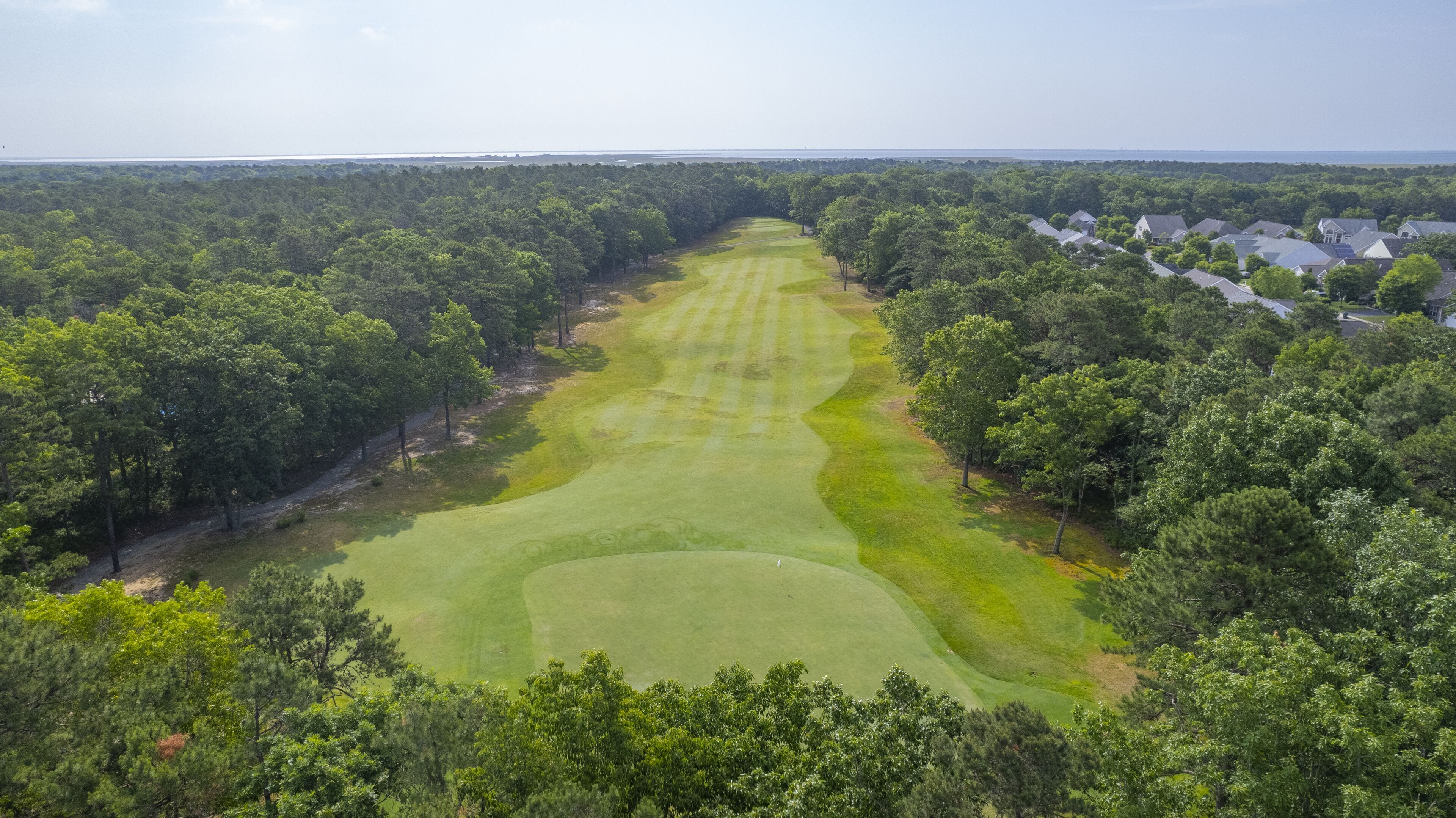 A golf course surrounded by dense forest and residential buildings.