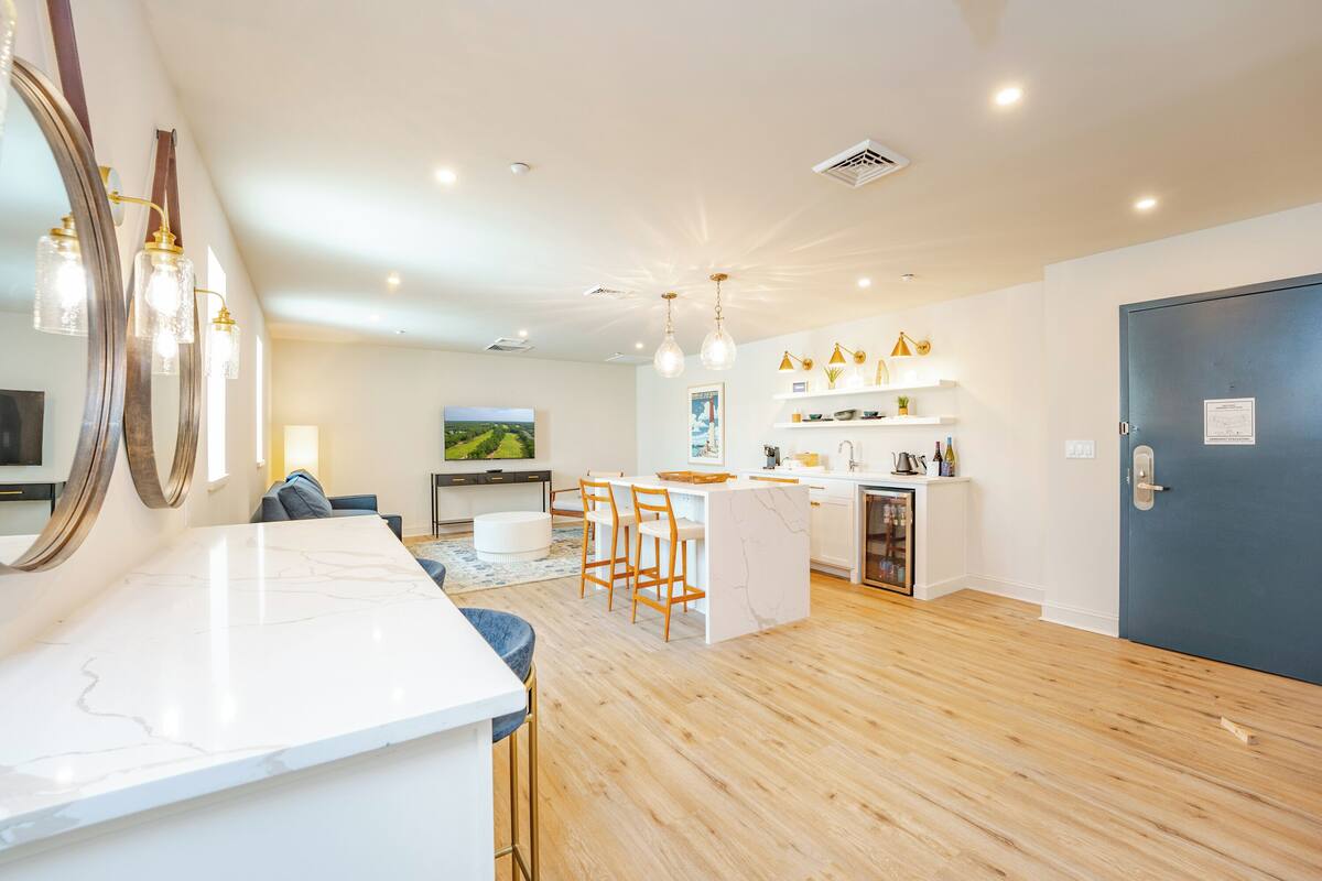 A modern kitchen with a marble countertop, wooden flooring, and pendant lighting.