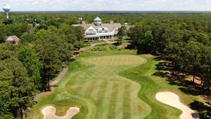 A golf course with a clubhouse, surrounded by dense trees and a clear sky.