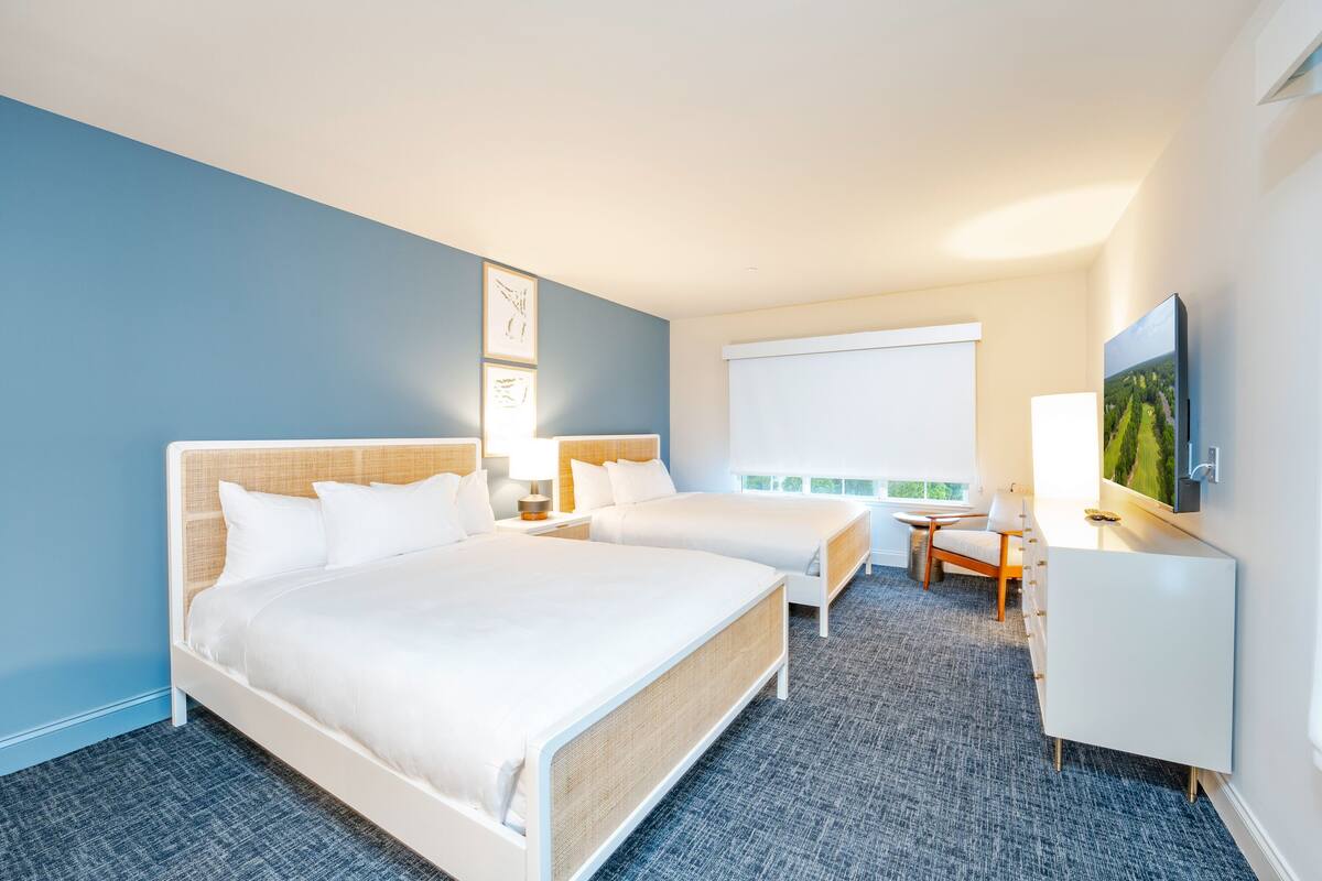 A hotel room with two beds, a desk, a chair, and a TV.