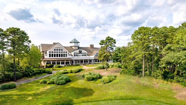 A large, two-story building with a prominent tower and multiple windows, surrounded by lush greenery and a well-maintained lawn.