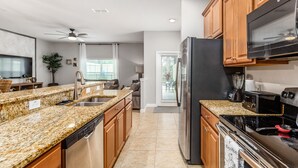 A modern kitchen with granite countertops, stainless steel appliances, wooden cabinets, and a ceiling fan.
