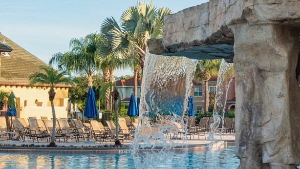A pool area with a waterfall feature, lounge chairs, and palm trees.