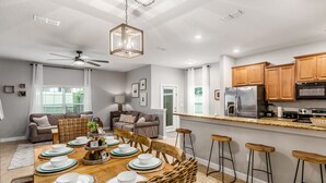 A modern kitchen with wooden cabinets, a stainless steel refrigerator, and a bar area with stools.