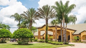 A yellow building with a tiled roof, surrounded by palm trees and well-maintained lawns.