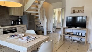 Uma cozinha moderna com fogão embutido, mesa de jantar com cadeiras, escada e rack para televisão com dispositivos eletrônicos.
