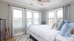 Ein Schlafzimmer mit einem Bett, einem Deckenventilator und großen Fenstern.