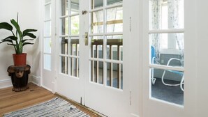 Eine weiße Tür mit mehreren Glasscheiben, ein Blumentopf und ein Streifenmuster-Teppich auf Holzdielen.