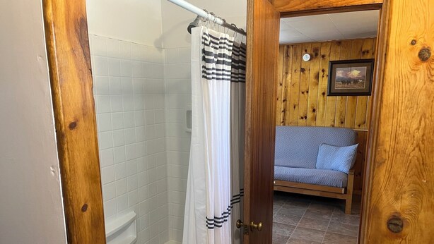 Une porte à cadre en bois donnant sur une salle de bain équipée d’un rideau de douche et d’une baignoire.