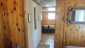 Un couloir en bois mène à un espace repas comprenant une table et des chaises, un tapis sur le sol et un lit au premier plan.