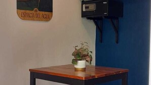A dining area with a wooden table and two matching chairs, a hanging light fixture, a wall-mounted shelf, and a decorative piece with a parrot. - Estancia del Agua (Xul-Ha)