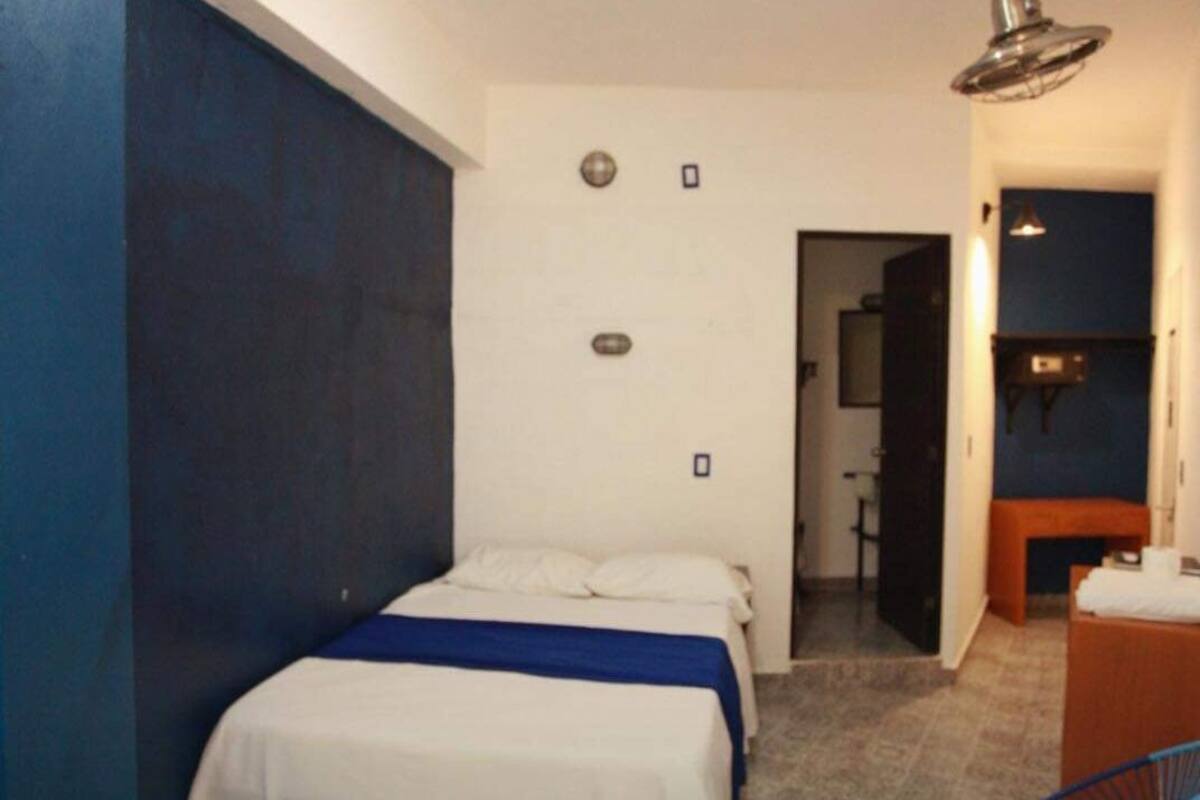 A bedroom with a bed, a chair, a desk, and a bathroom visible through an open door.