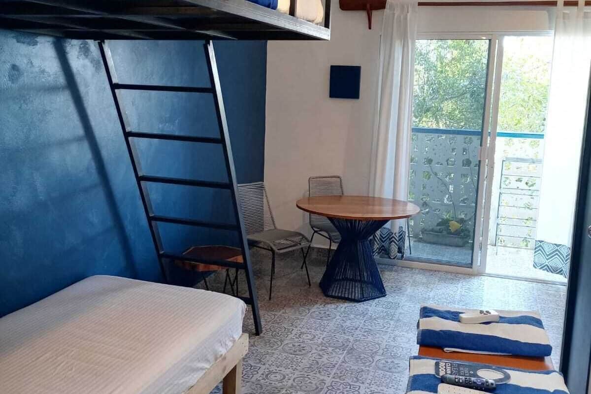 A dorm-style room with bunk beds, a small table, and a chair.