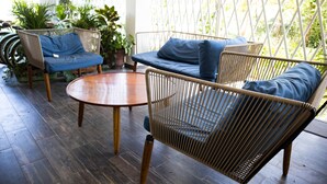 A wooden floor, wicker furniture, and potted plants in a room with a lattice wall. - Estancia del Agua (Xul-Ha)