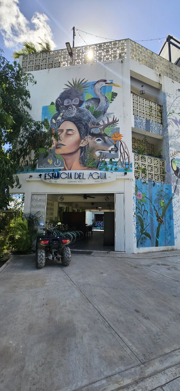 A building with a mural of a woman and a bird, a sign reading "Estancia del Agua," and an ATV parked in front. - Estancia del Agua (Xul-Ha)