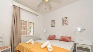 A hotel room with two beds, a window with curtains, a ceiling fan, and wall-mounted lamps.