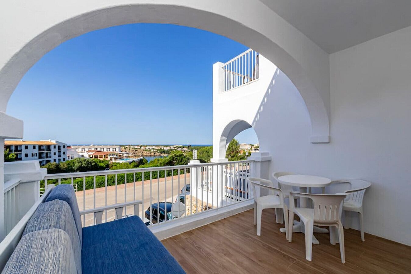A balcony with a view of the sea, white furniture, and a wooden floor.