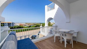 A balcony with a view of the sea, white furniture, and a wooden floor.