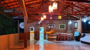 Una habitación amplia con techo alto, vigas a la vista y piso de baldosas pulidas. Varias mesas y sillas dispuestas para comer o conversar.