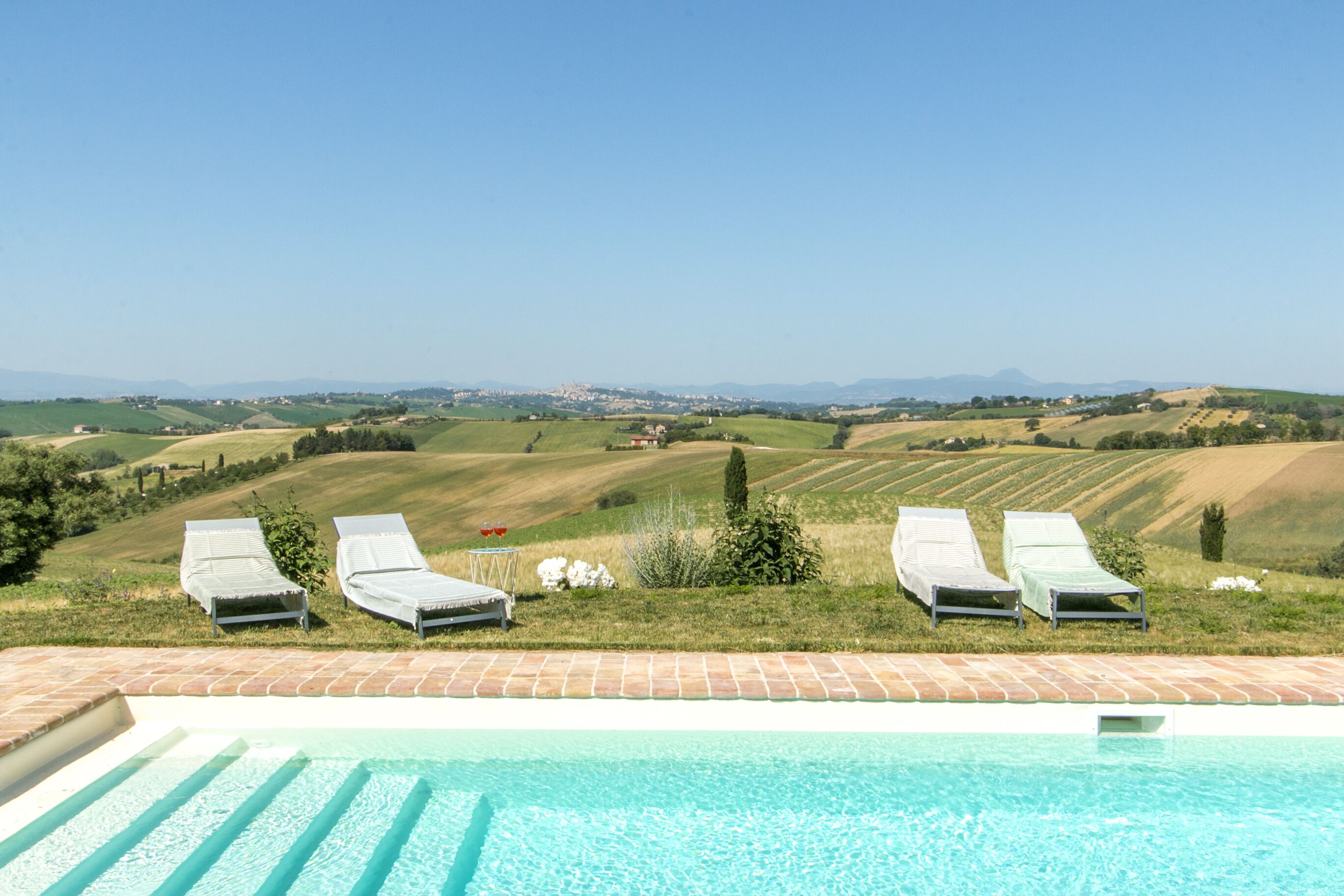 A pool with lounge chairs and a view of rolling hills and distant mountains.