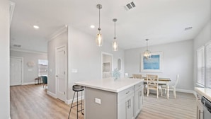 A modern kitchen with a central island, pendant lights, and a dining area with a table and chairs.