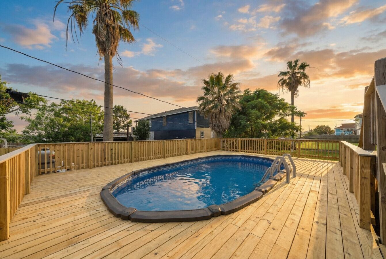 A wooden deck with a swimming pool, surrounded by a wooden fence and palm trees.