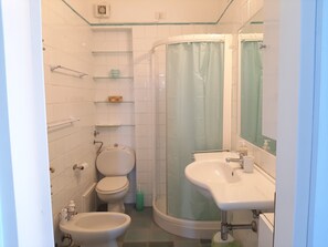 Une salle de bain comprenant des toilettes, un bidet, un lavabo et une douche à parois de verre.
