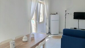 A compact living space with a wooden dining table, white chairs, a blue sofa, a white refrigerator, and a mounted TV. - Overlooking the sea Santa Teresa Gallura (Santa Teresa di Gallura)