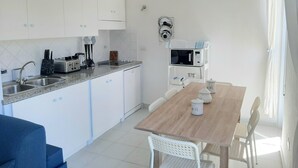 A compact kitchen with white cabinets, a microwave, and a sink. There is a dining table with chairs and a blue couch. - Overlooking the sea Santa Teresa Gallura (Santa Teresa di Gallura)
