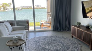 Un salon moderne doté d’une grande fenêtre donnant sur un plan d’eau, d’un canapé, d’une table basse et d’un téléviseur à écran plat.