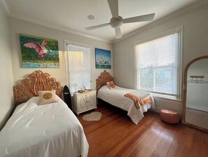 Une chambre avec deux lits, un ventilateur de plafond et des œuvres d’art accrochées aux murs.