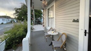Une véranda avec une balustrade blanche, deux fauteuils en osier, une petite table ronde et un luminaire suspendu.