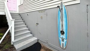 Une maison avec une porte rose, un escalier menant à un porche et une planche de surf fixée au mur extérieur.