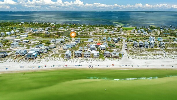 Vista aérea de una zona residencial costera con casas, una playa y cielo despejado.