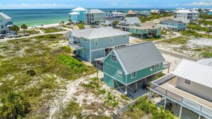 Una zona residencial costera con varias casas, algunas construidas sobre pilotes, cerca de una playa bajo cielos despejados.