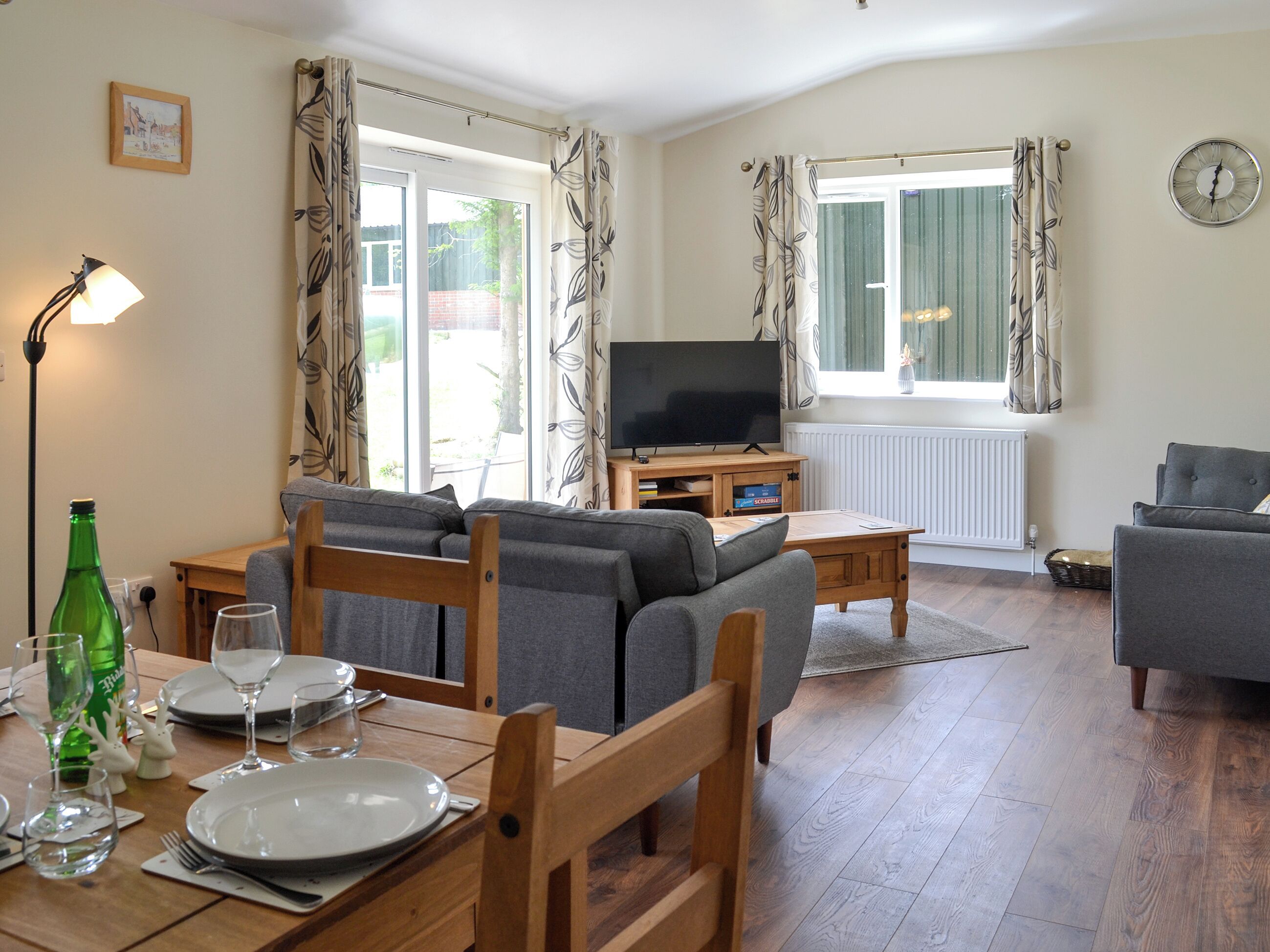 A living room with a sofa, television, dining table set, and large windows.