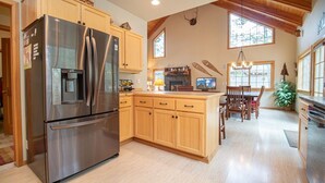 A kitchen with wooden cabinets, a stainless steel refrigerator, a water dispenser, and a dining area with a table and chairs. - Sunriver 3 bedroom home, new hot tub, 8 SHARC passes (Sunriver)