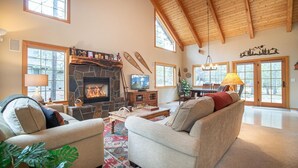 A cozy living room with a stone fireplace, comfortable seating, and large windows. - Sunriver 3 bedroom home, new hot tub, 8 SHARC passes (Sunriver)