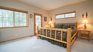A bedroom with a wooden bed, two bedside tables with lamps, a large window, and a door.
