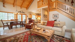 A spacious living room with a high ceiling, wooden furniture, a dining area, and a staircase leading to an upper level. - Sunriver 3 bedroom home, new hot tub, 8 SHARC passes (Sunriver)