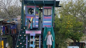Estructura de juegos infantiles con tobogán y pared de escalada, junto a una piscina.