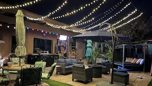 Un patio al aire libre con luces colgantes, mobiliario de mimbre, una parrilla y una zona de bar.