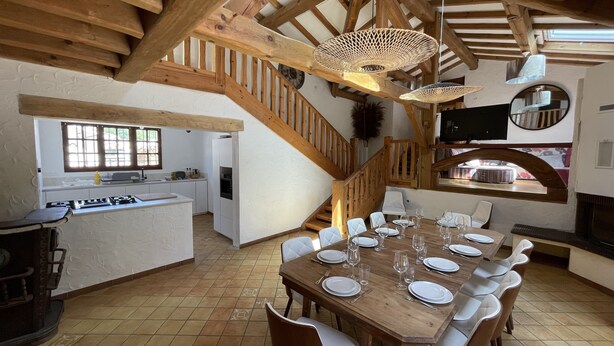A spacious dining area with a wooden table set for six, surrounded by white chairs. A wooden staircase with a railing leads to an upper level. - Semi-detached house in gujan la hume (Gujan-Mestras)