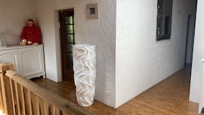 A hallway with a wooden floor, white textured walls, a large white vase, a red statue, and a mirror on the wall. - Semi-detached house in gujan la hume (Gujan-Mestras)
