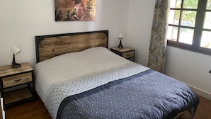 A bedroom with a wooden headboard, a patterned bedspread, a nightstand with a lamp, and a painting on the wall. - Semi-detached house in gujan la hume (Gujan-Mestras)