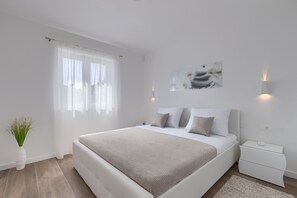 Ein modernes Schlafzimmer mit einem großen Bett, einem Nachttisch, einer Wandleuchte und einem Fenster mit durchsichtigen Vorhängen.