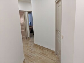 Un passadís estret amb terra de fusta que condueix a una habitació amb un llit i una nitzeta.