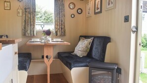 A cozy interior with a wooden table, a black sofa, and a small stove. - This cosy and quiet Shepherd’s Hut is a great way to unwind. (Frampton-on-Severn)