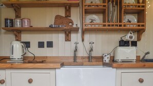 A kitchen with wooden shelves, a kettle, a toaster, and a sink. - This cosy and quiet Shepherd’s Hut is a great way to unwind. (Frampton-on-Severn)